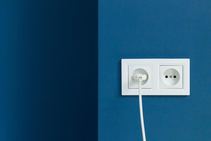 Hvit elektrisk plugg i dobbel stikkontakt på blå vegg.