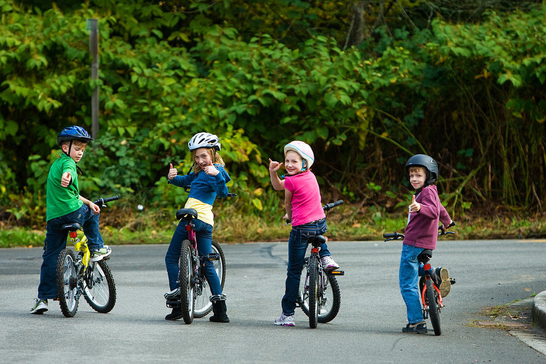 Barn med hjelm og sykkel som viser tommel opp.