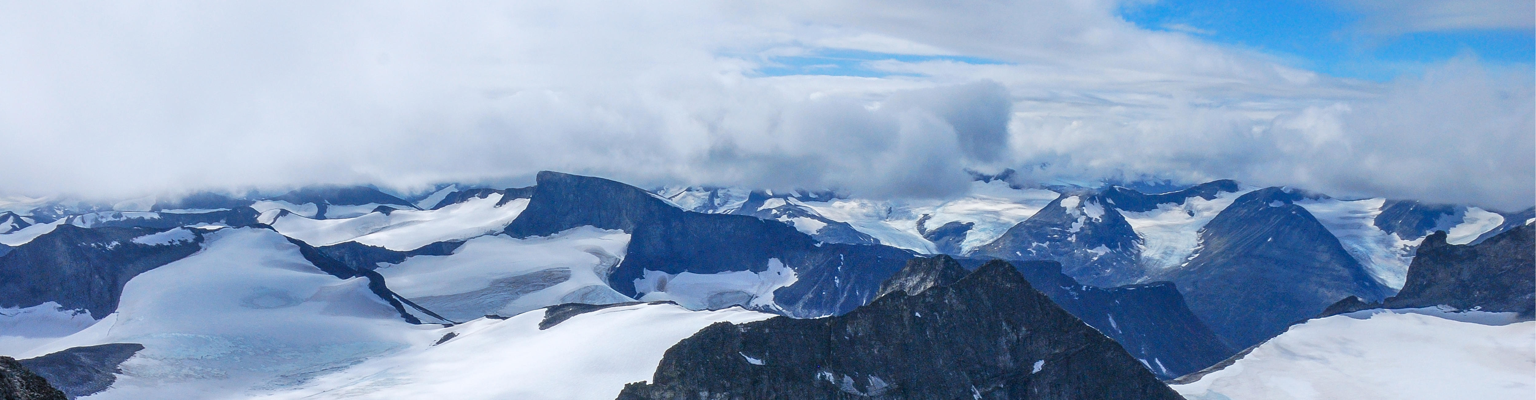 Fjellområde med isbre. Solfylt vær med noen skyer. Utsikt fra det høyeste fjellet i Norge, Galdhøpiggen