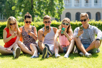 Studenter i parken  med mobiltelefon.