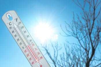 Thermometer som viser lav temperatur med blå himmel og sol i bakgrunnen.