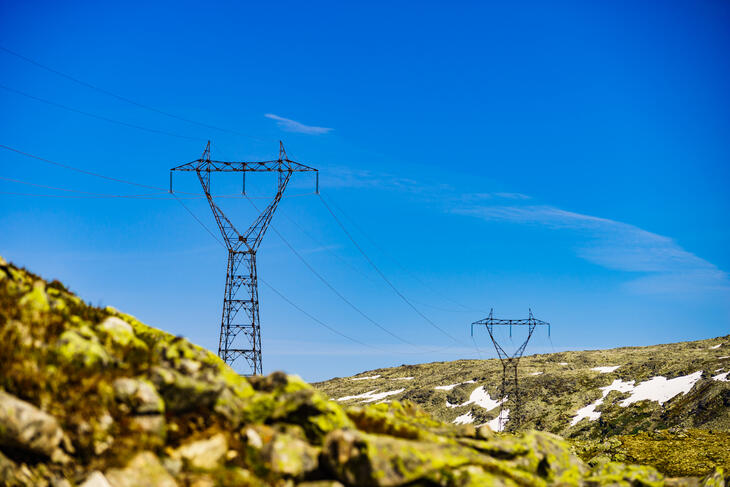 Elektrisitetsoverføringsmaster i norsk fjellandskap med blå himmel.