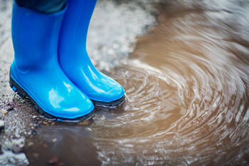 Blå gummistøvler i sølepytt i regnvær.