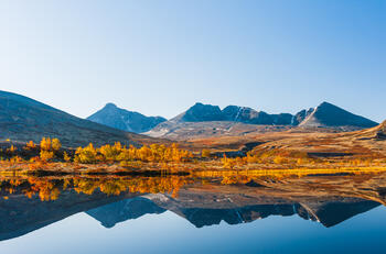 Utsikt til Dovre Nasjonalpark med klart vann, fjelltopper og høstfarger i fjellet.