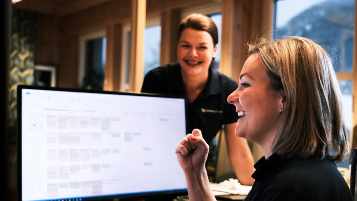 To kvinnelige kolleger som smiler foran en PC-skjerm.